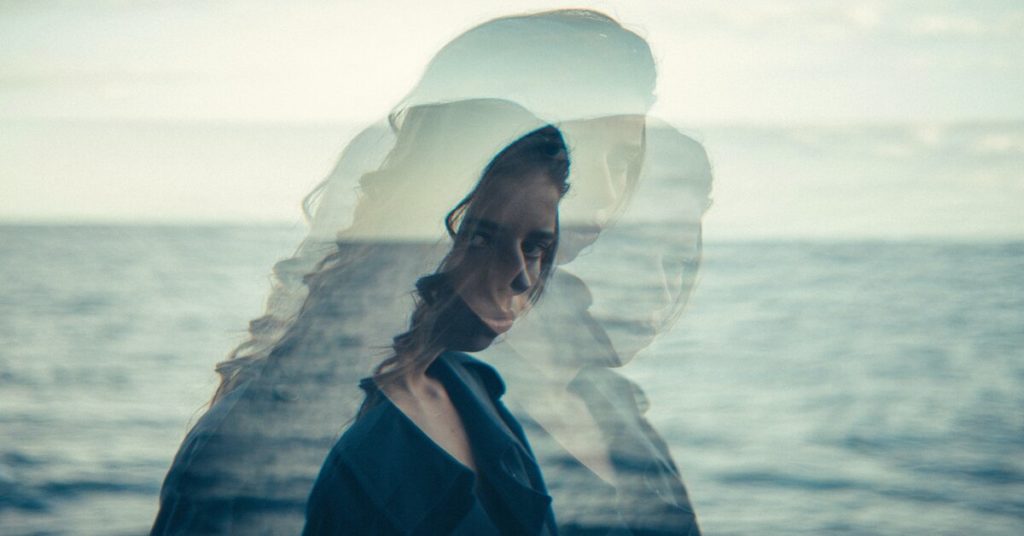 A woman with curly brown hair is shown with two shadowy images of herself, against an ocean backdrop, illustrating the concept of intuition.