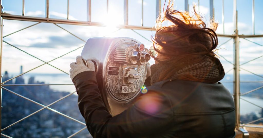 A woman is using a telescope at the top of a tall building, illustrating the concept of curiosity.