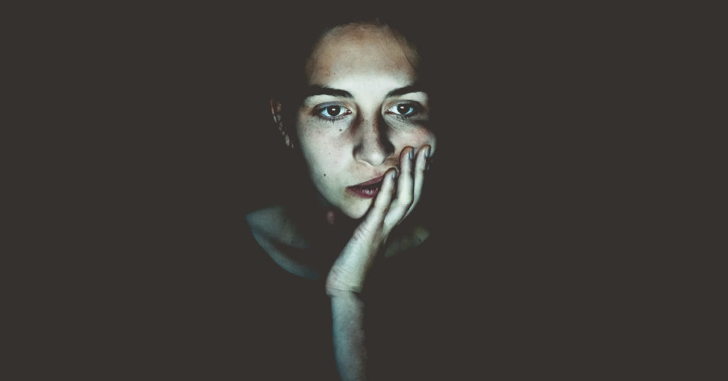 A woman is shown holding her face in her hand, against a dark background, illustrating the concept of wrestling with doubt.