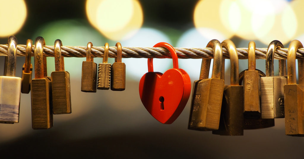Padlocks hang on a rope. The central lock is red and heart-shaped, illustrating Amor Fati.
